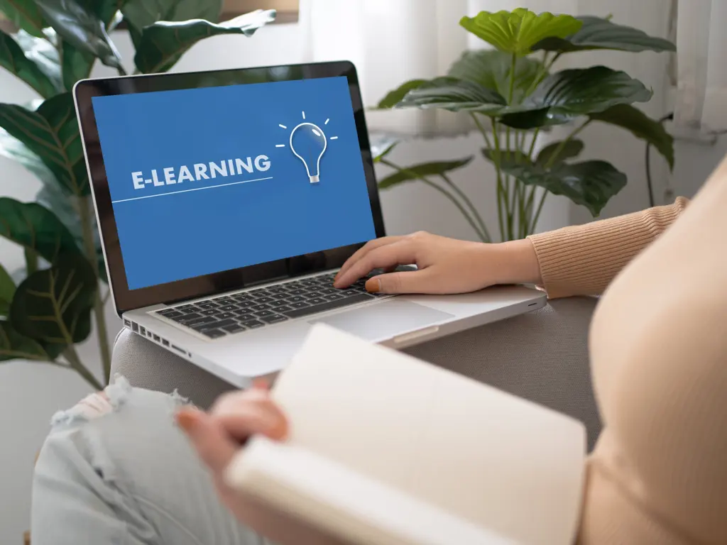 Frau sitzt mit Notizbuch vor einem Laptop mit E-Learning-Bildschirm – Symbolbild für Online-Kurse zur Website-Erstellung für Selbstständige